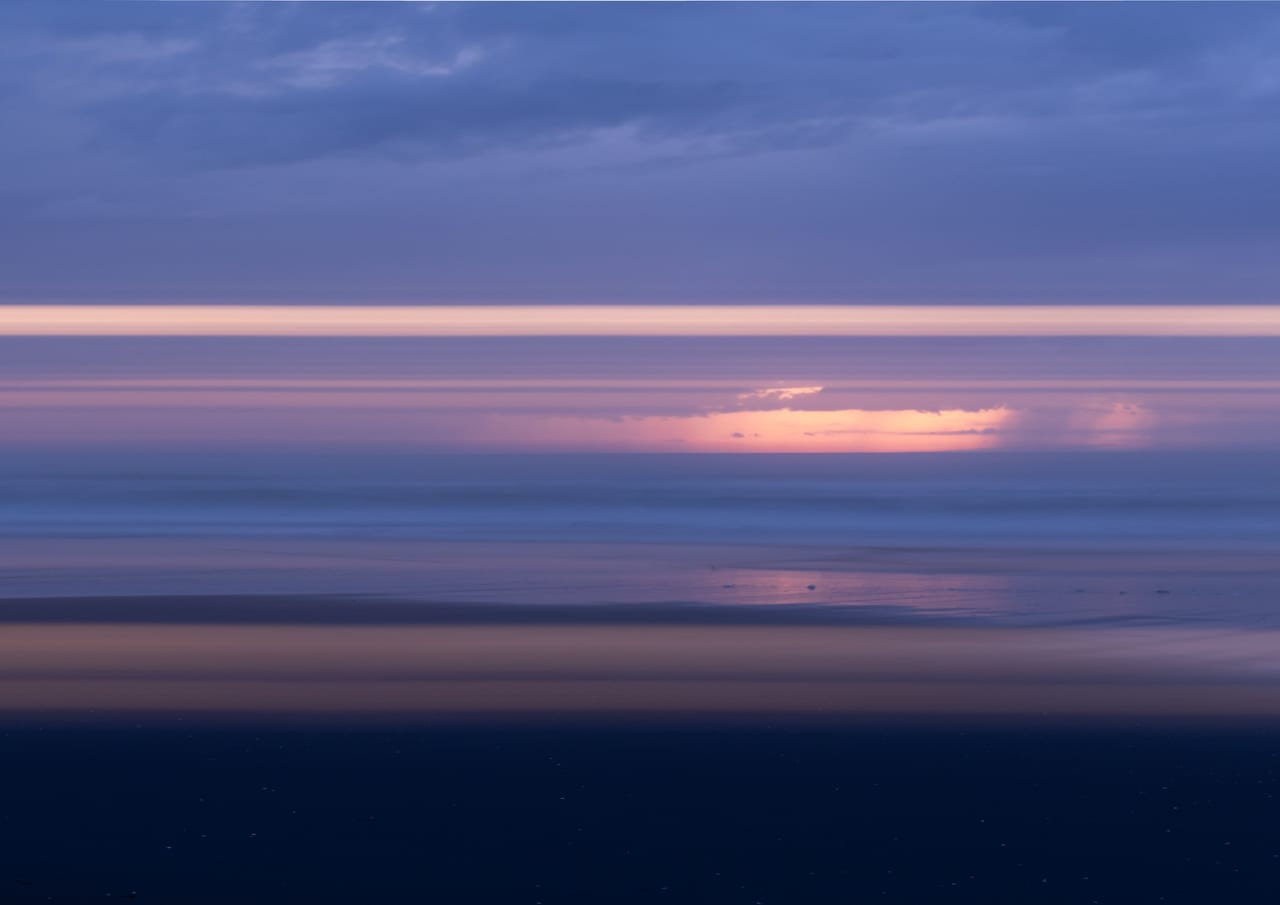 Soft pink sunset light above blue coastal water.